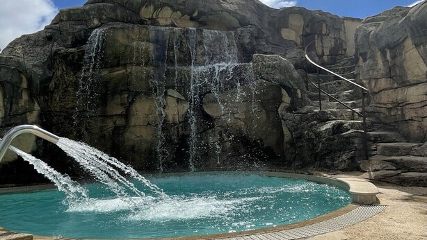 A pool with a waterfall feature, surrounded by rocky terrain and a clear blue sky. - MOBILE HOME R10 ALL COMFORT - 5* CAMPSITE (Quimper)