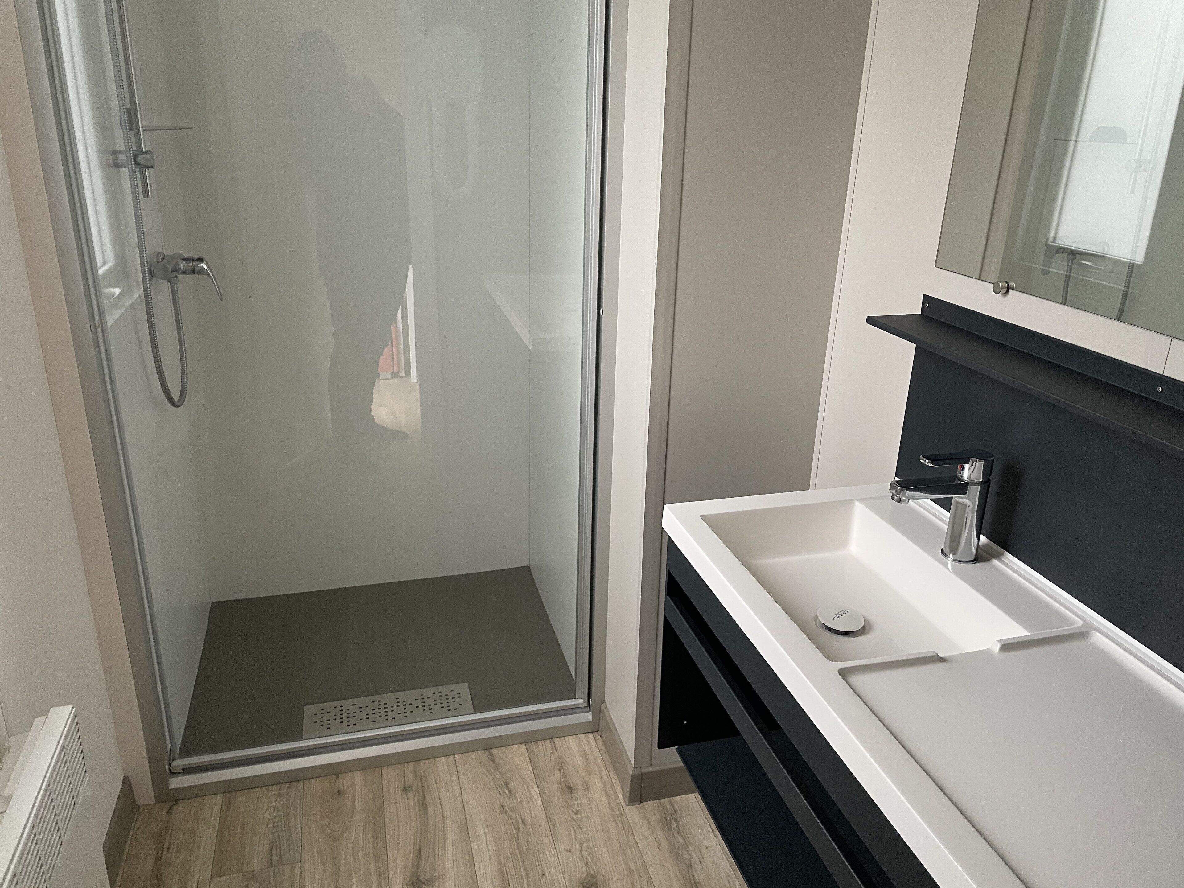 A modern bathroom with a glass shower enclosure, a white sink, and a black countertop.