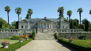 A large, stately building with a symmetrical facade, a central entrance with steps, and a formal garden with neatly trimmed hedges and palm trees. - MOBILE HOME R10 ALL COMFORT - 5* CAMPSITE (Quimper)