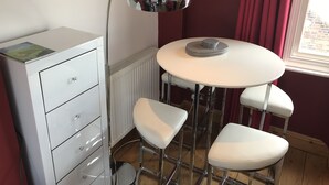 A compact room with a white desk, a round table with a stack of plates, and two white bar stools. - Laines Loft - cosy flat in the centre of The Laines, with private sun terrace (Brighton)