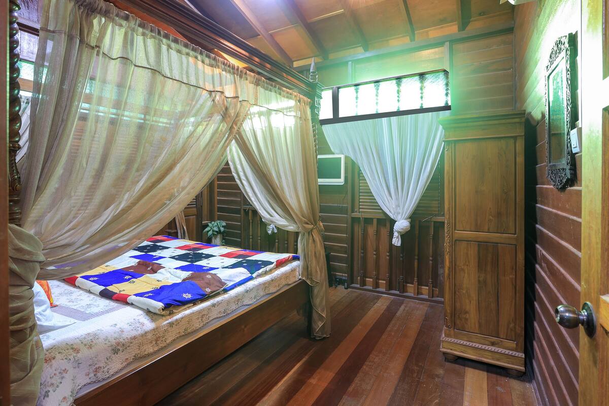 Een houten slaapkamer met een bed, gordijnen en een houten kledingkast.