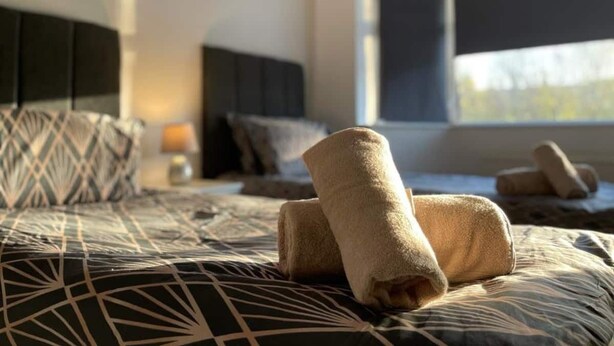 Uma cama bem arrumada com toalhas dobradas, um cobre-leito estampado e uma mesa de cabeceira com abajur.