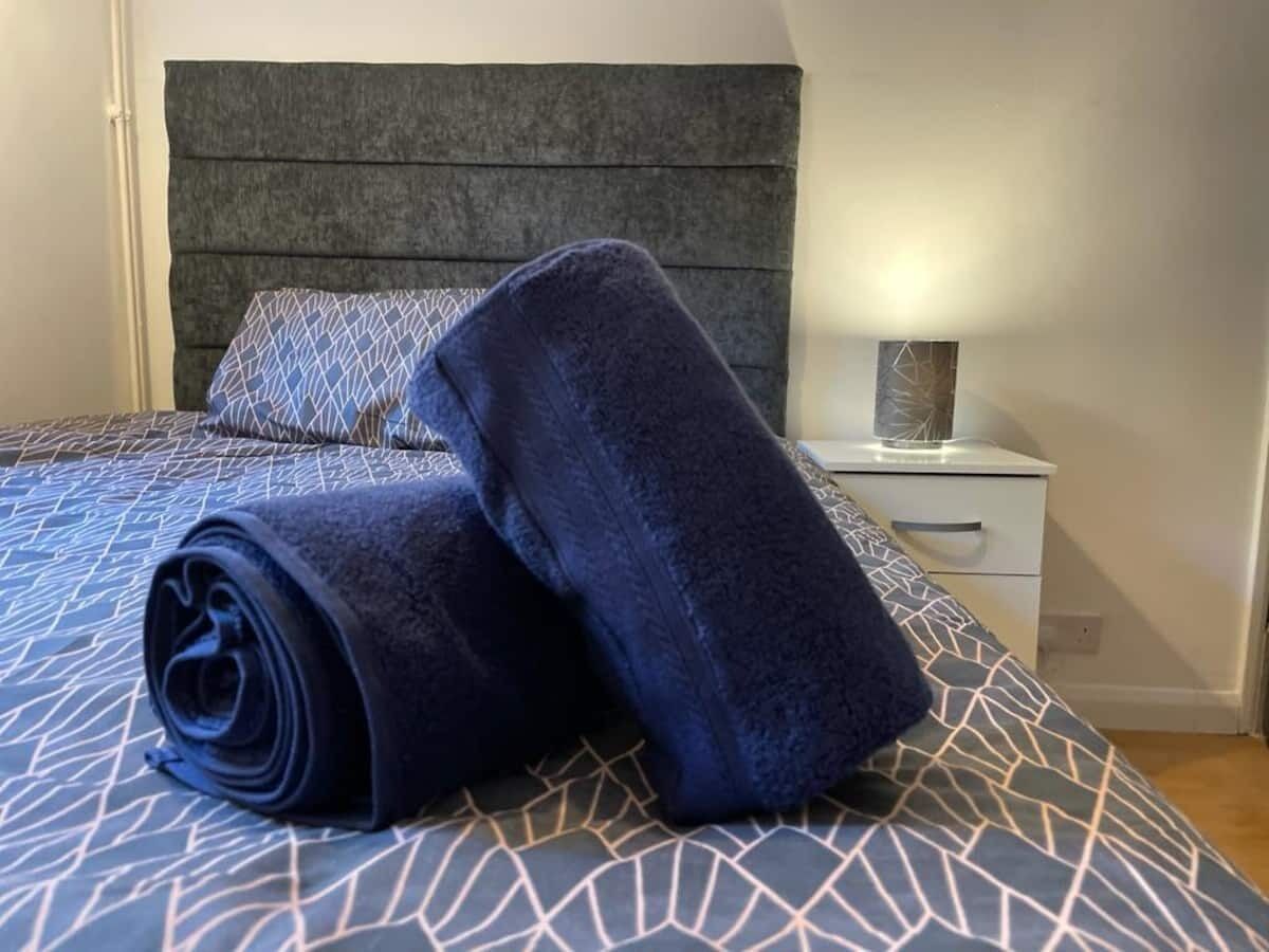 A neatly made bed with a patterned bedspread and two rolled towels on it.