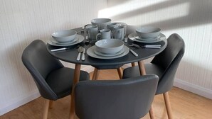 Mesa de jantar redonda com quatro cadeiras pretas, posta com pratos, tigelas e copos.