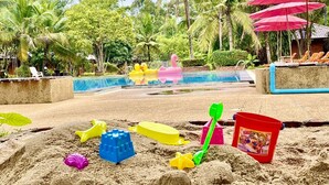 A sandy area with beach toys, a pool, and palm trees.