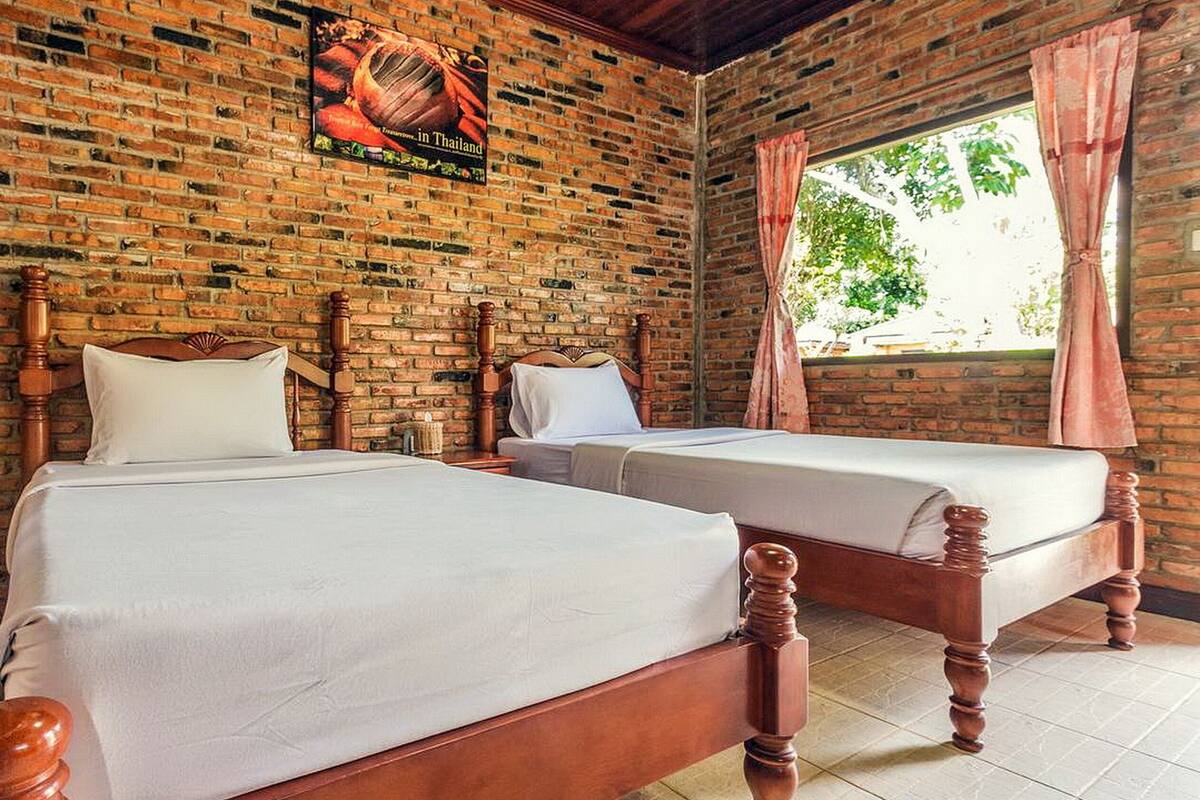 A room with two wooden beds, a brick wall, and a window with curtains.