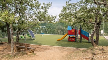 Explore the playground area, featuring a swing set, slide, and climbing structure, surrounded by trees and a fence.