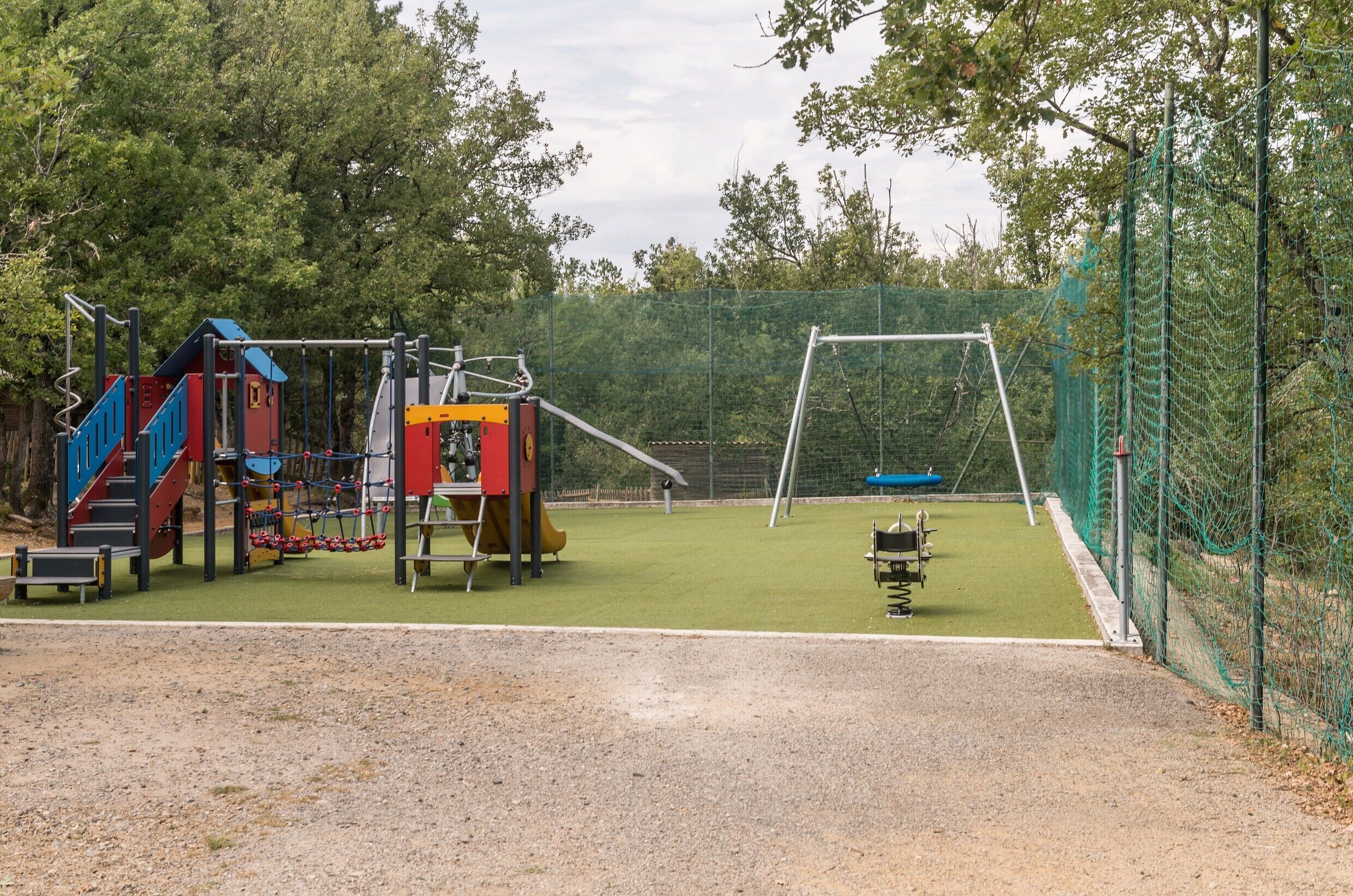 Een speeltuin met een klimconstructie, schommels en een omheind gedeelte.