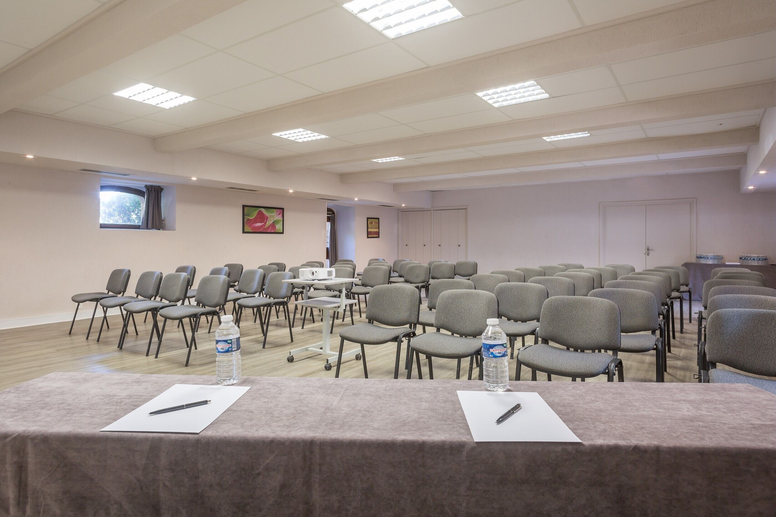 Una sala de conferències amb files de caires, taules amb ampolles d'aigua i una pantalla de projector.