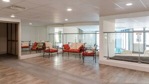 Une pièce spacieuse dotée d’un plancher en bois, d’une cloison en verre et d’un coin salon avec des fauteuils rouges et beiges.