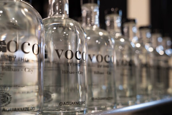 Una fila de botellas de vidrio transparente con etiquetas, presumiblemente con bebidas, dispuestas en una estantería.