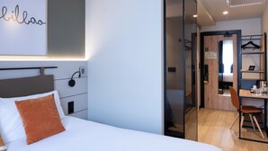 A modern hotel room with a bed, a desk, and a wardrobe.