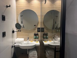 Een moderne badkamer met twee wasbakken, ronde spiegels en een glazen douchewand.