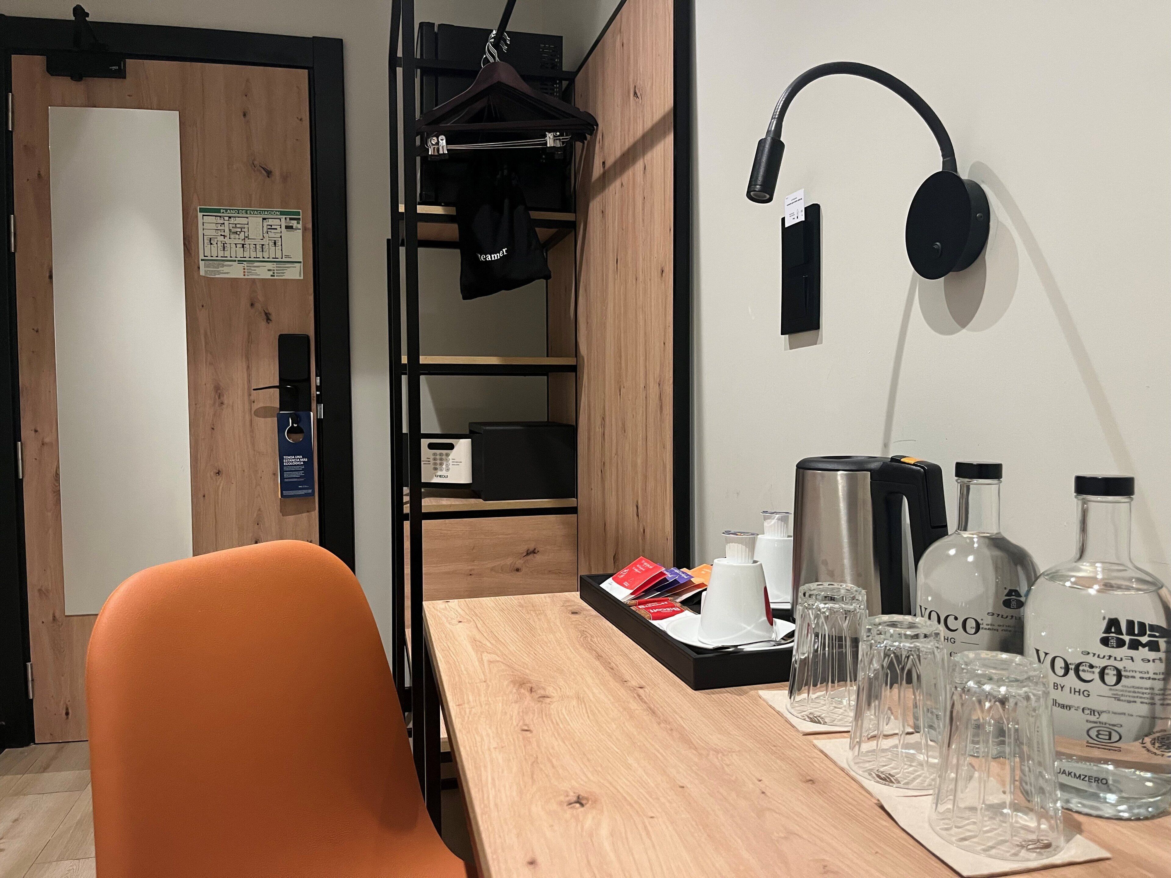 A room with a wooden table, a black hanger, a black speaker, and a whiteboard with text.