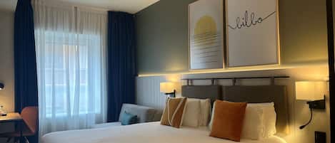 A hotel room with a large bed, two bedside tables with lamps, a desk with a chair, and a window with curtains.