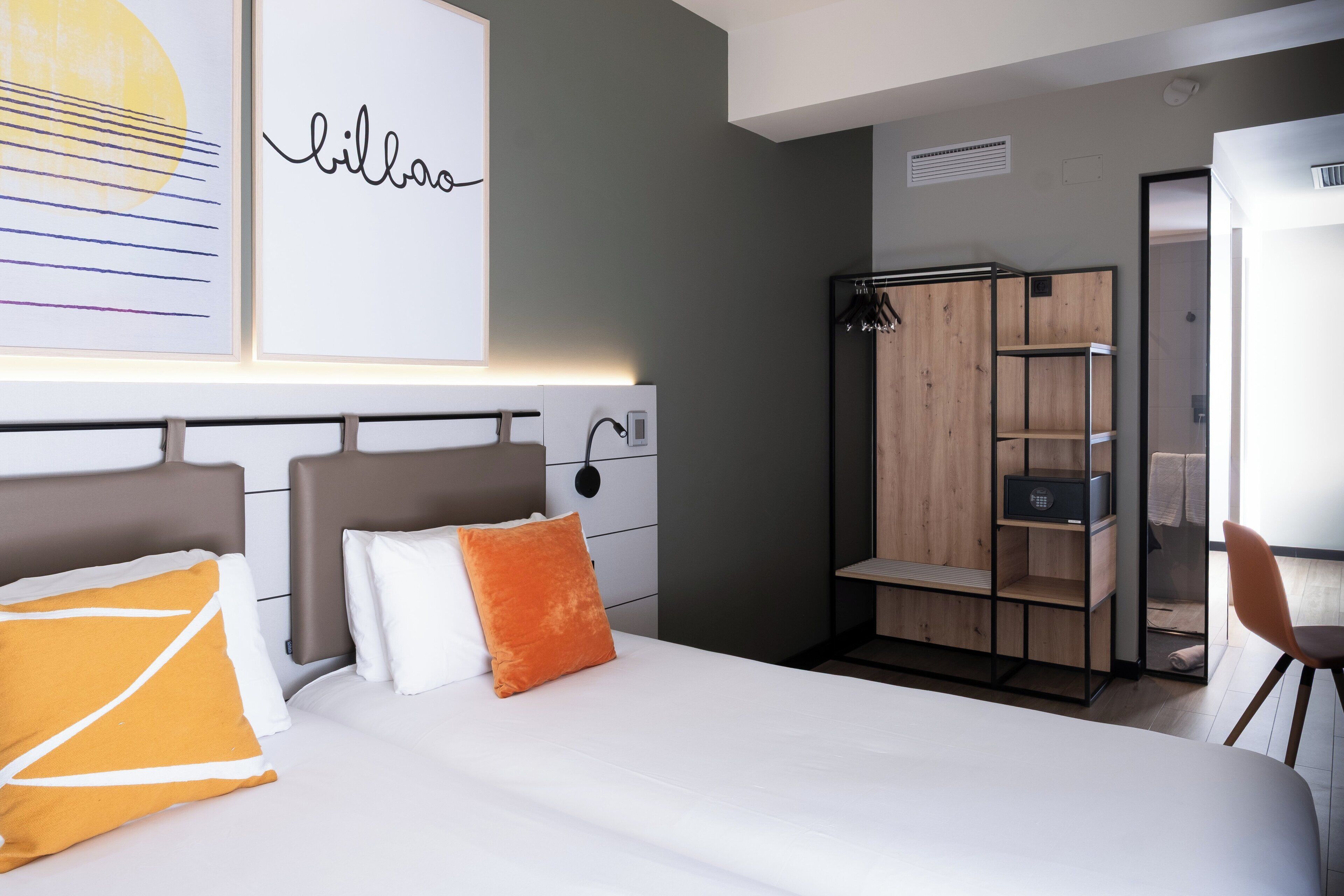 A modern hotel room with a large bed, a wardrobe, and a desk.