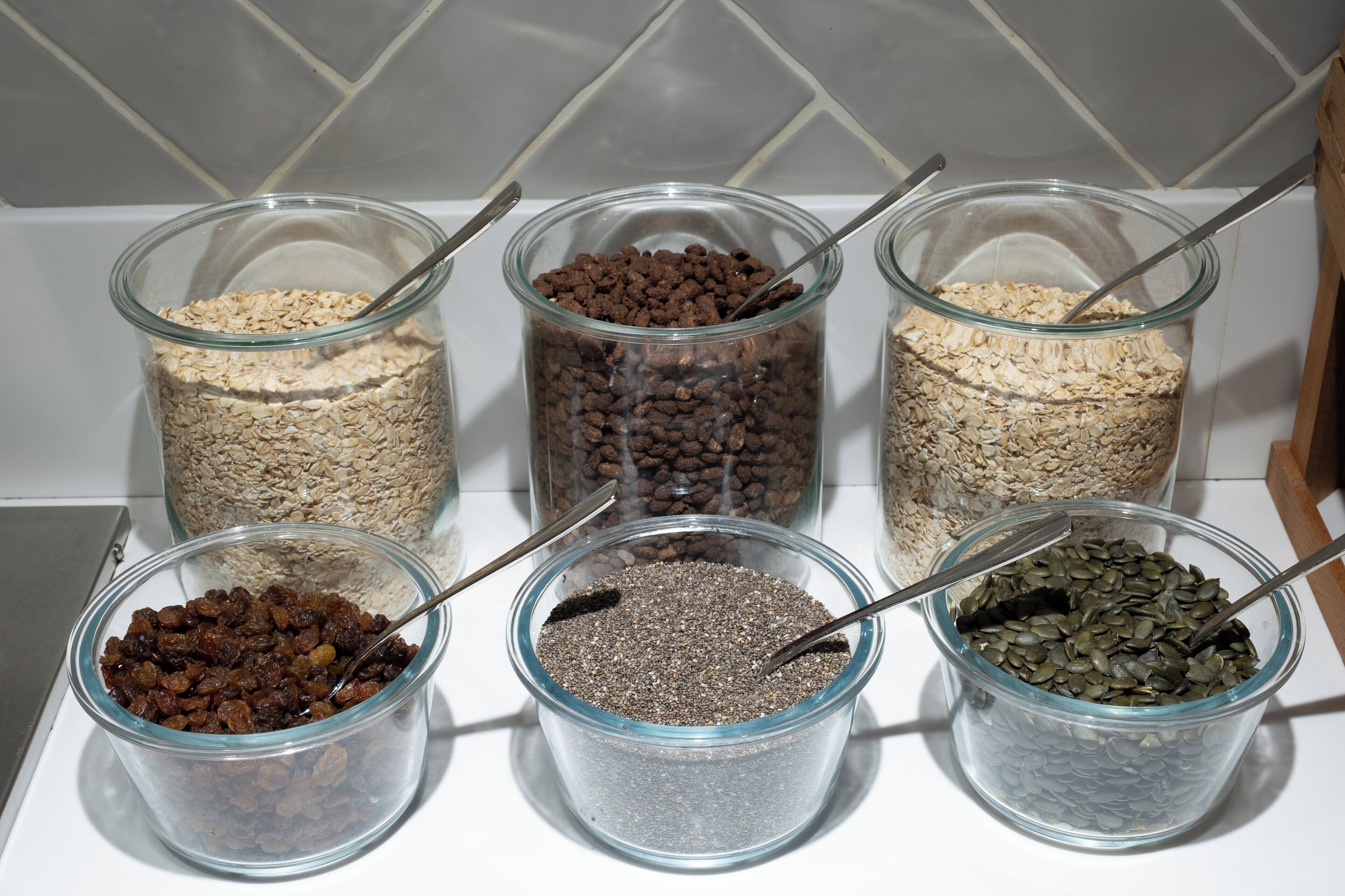 Five glass jars containing different grains and seeds on a kitchen counter.