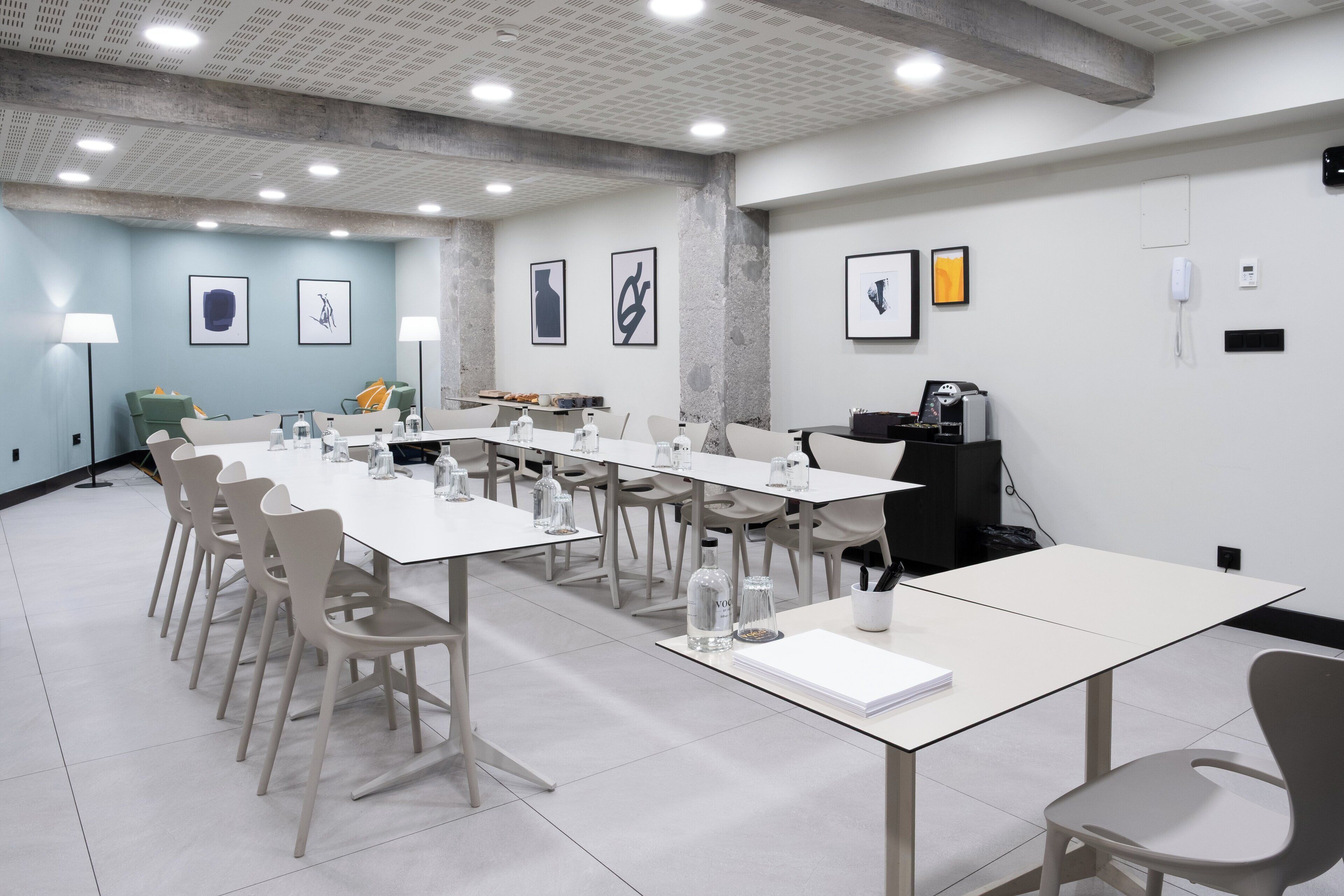 Un salón de conferencias con mesas y sillas blancas, un proyector y cuadros en las paredes.
