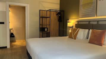 Habitación de hotel con una cama grande, un armario, un escritorio y una lámpara de pared.