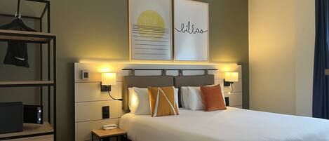 Una habitación de hotel moderna con una cama grande, mesitas de noche, un armario y una obra de arte colgada en la pared.