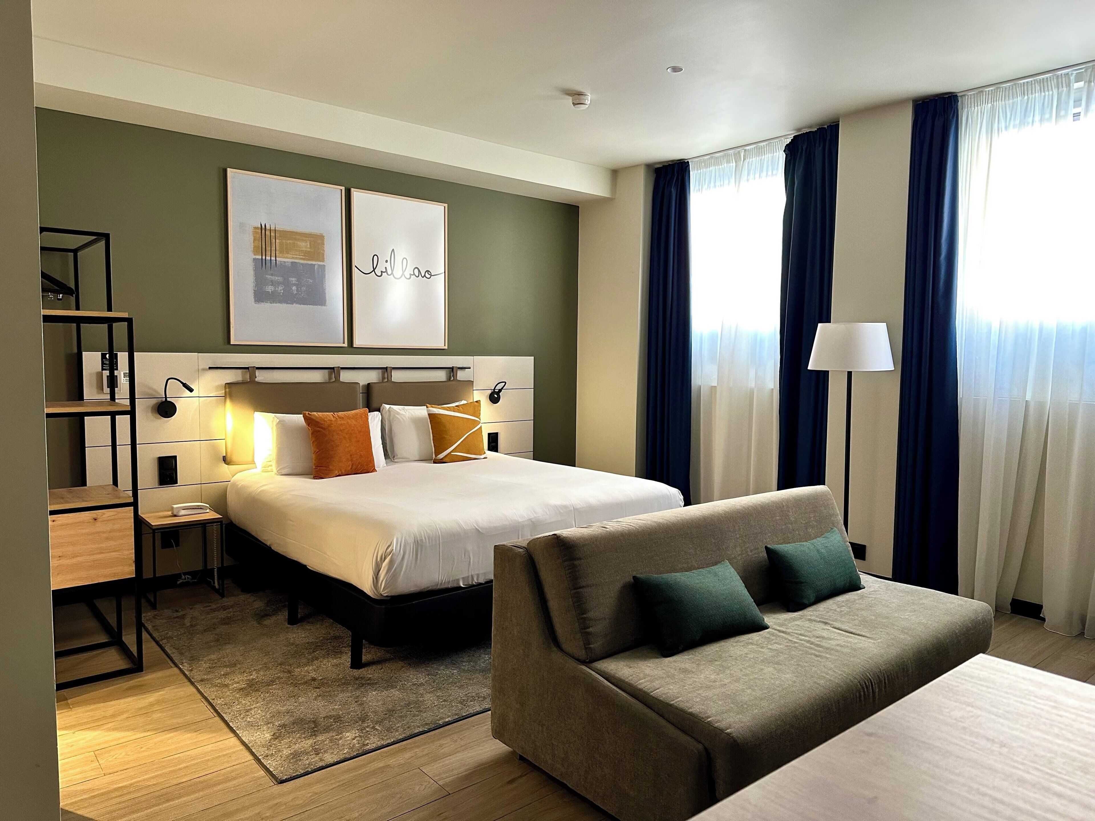 Una habitación de hotel con cama, sofá, escritorio y estantería.