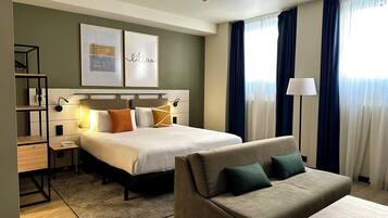 Una habitación de hotel con cama, sofá, escritorio y estantería.