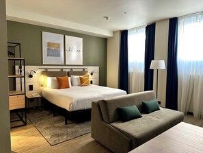 Una habitación de hotel con cama, sofá, escritorio y estantería.
