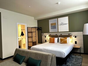 Habitación de hotel moderna con una cama grande, armario, zona de estar y obras de arte en las paredes.