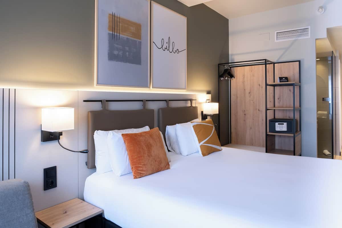 Ein modernes Hotelzimmer mit einem großen Bett, Nachttischlampen, einem hölzernen Kopfteil und einem Schrank mit Spiegel.