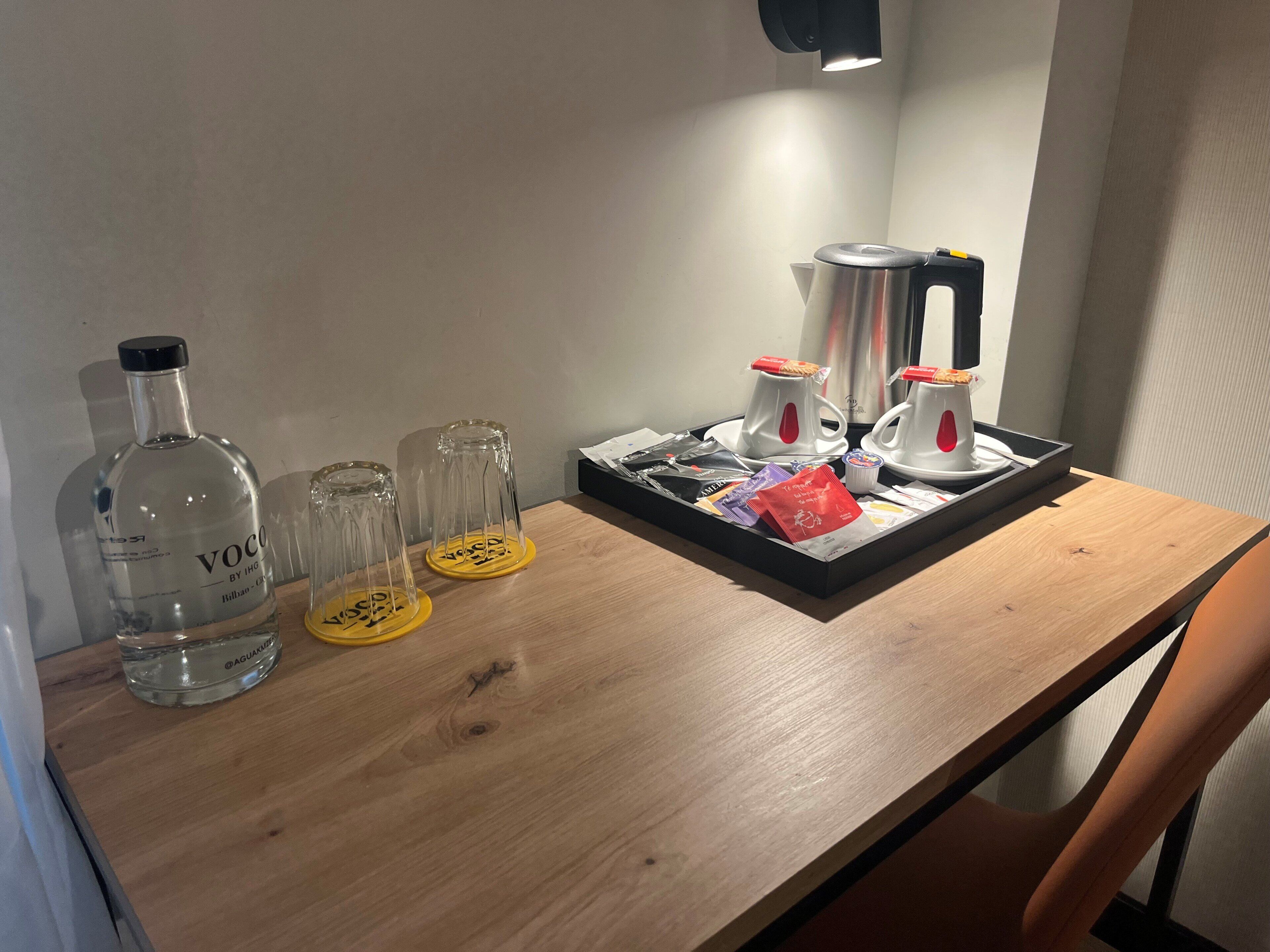 Una mesa de madera con una botella de agua, dos vasos, una bandeja con una tetera, hervidor y bolsitas de té.