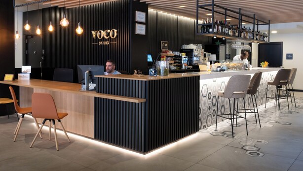 A modern bar area with a wooden reception desk, bar stools, and a variety of bottles and glasses on shelves.