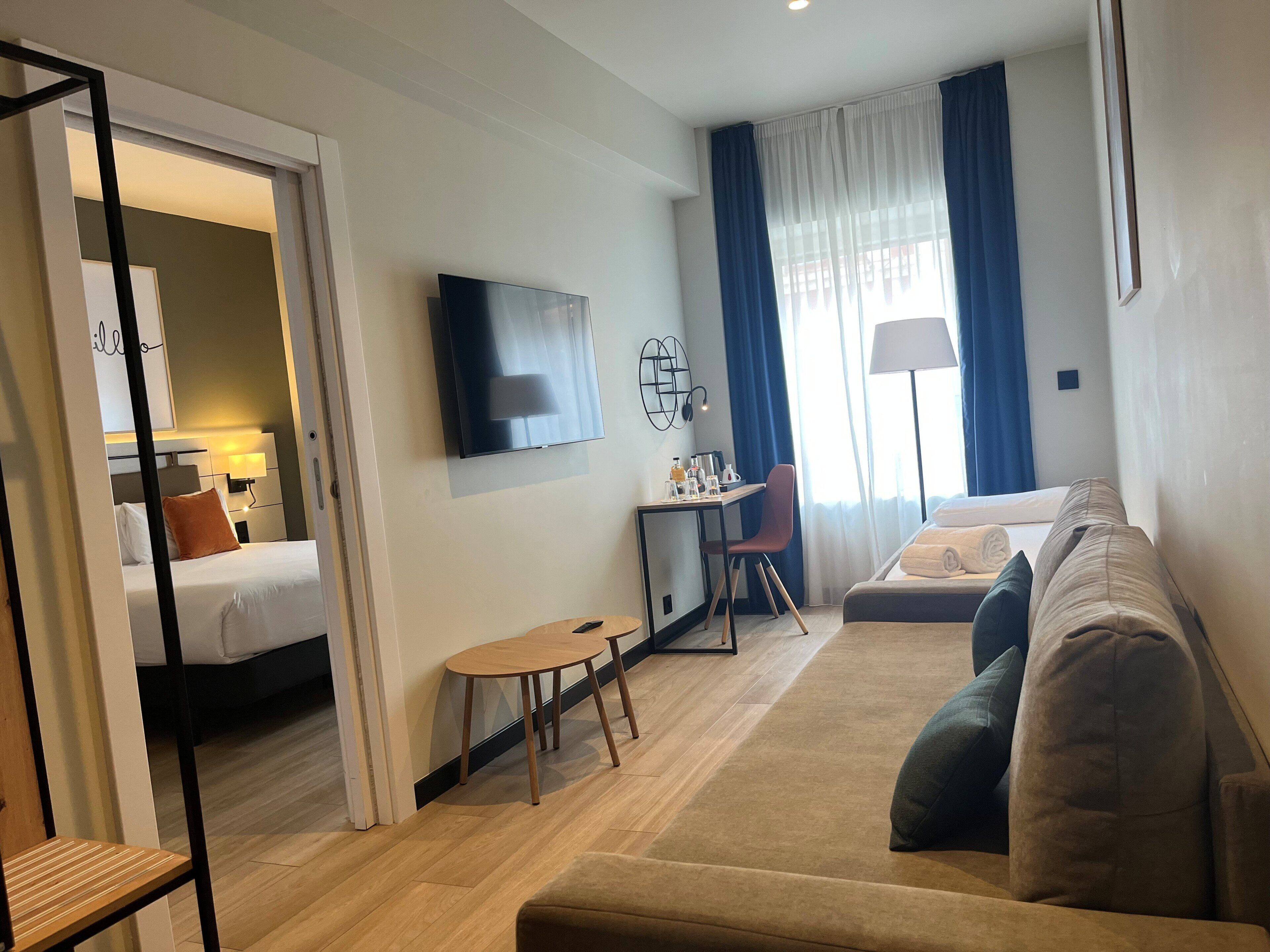 Een moderne hotelkamer met een bed, een bank, een bureau met stoel, een televisie en een raam met gordijnen.
