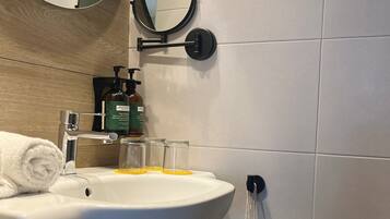 Un bany amb un lavabo blanc, dos miralls, una tovallola, un dosificador de sabó i una ampolla de vidre.