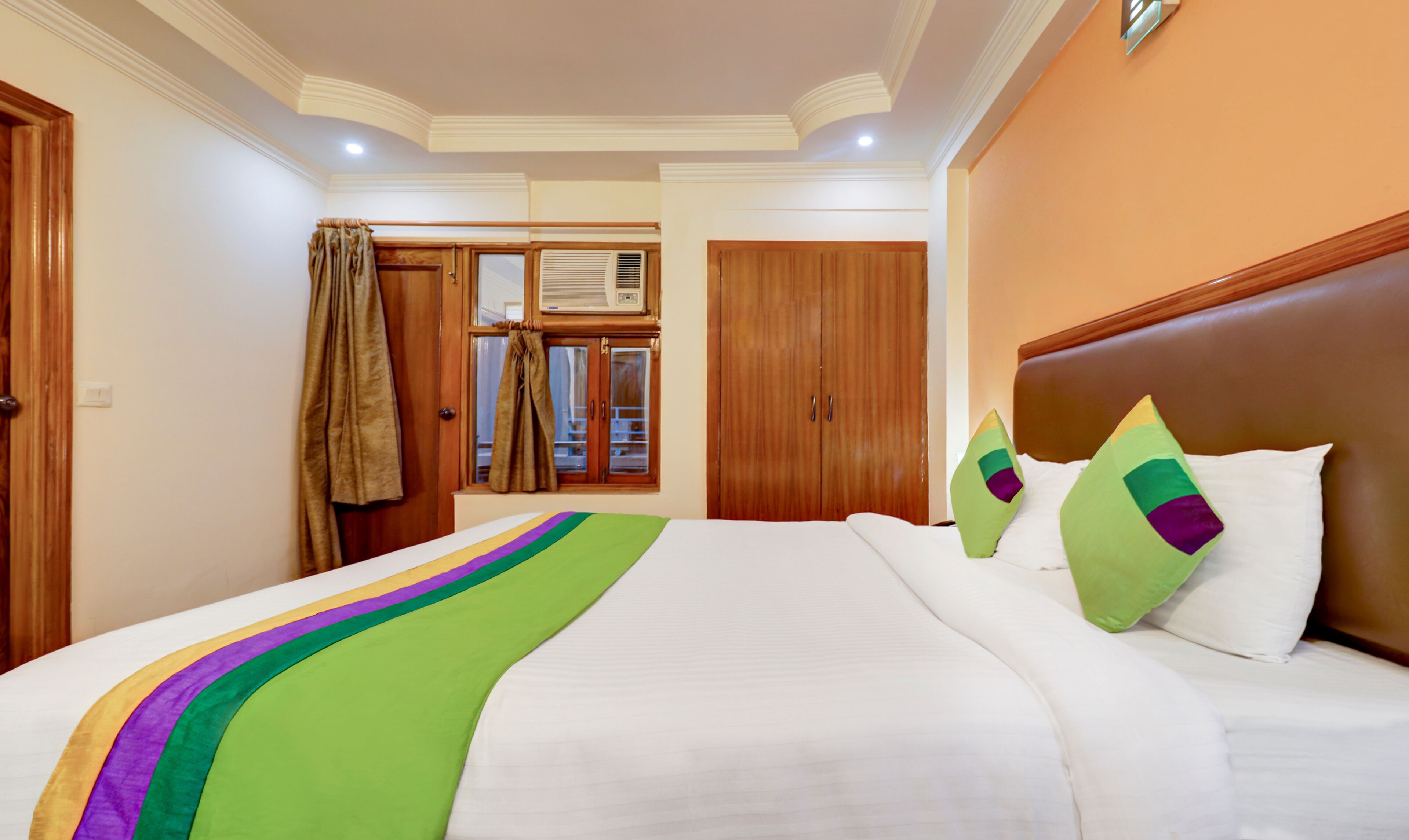 A hotel room with a large bed, wooden wardrobe, and a window with curtains.