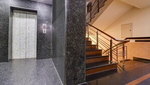 Un ascenseur moderne doté d’un panneau de commande, d’un escalier avec des rampes en métal et d’un mur orné d’un motif texturé.