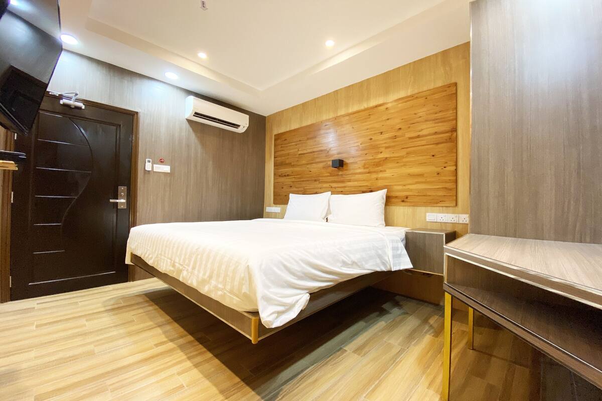 Ein modernes Hotelzimmer mit einem Holzkopfteil, einem Bett mit weißen Bettwäsche, einem Holzboden und einem an der Wand befestigten Fernseher.