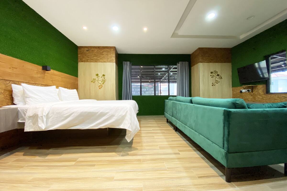 Ein Hotelzimmer mit Bett, einem grünen Sofa, einem Holzkopfstück, einem Flachbildfernseher und einem Fenster mit Vorhängen.