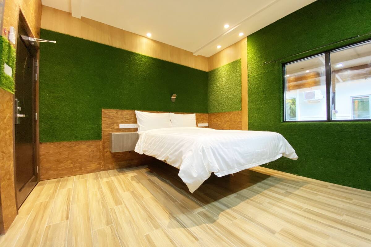 Ein Schlafzimmer mit Bett, grüner Wand, Holzwandverkleidung und einem Fenster.
