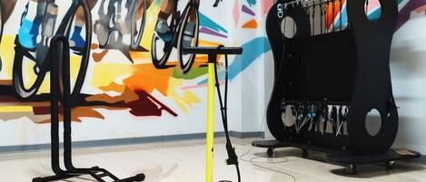 A stationary bike, a yellow exercise machine, and a black rack with tools against a colorful mural.