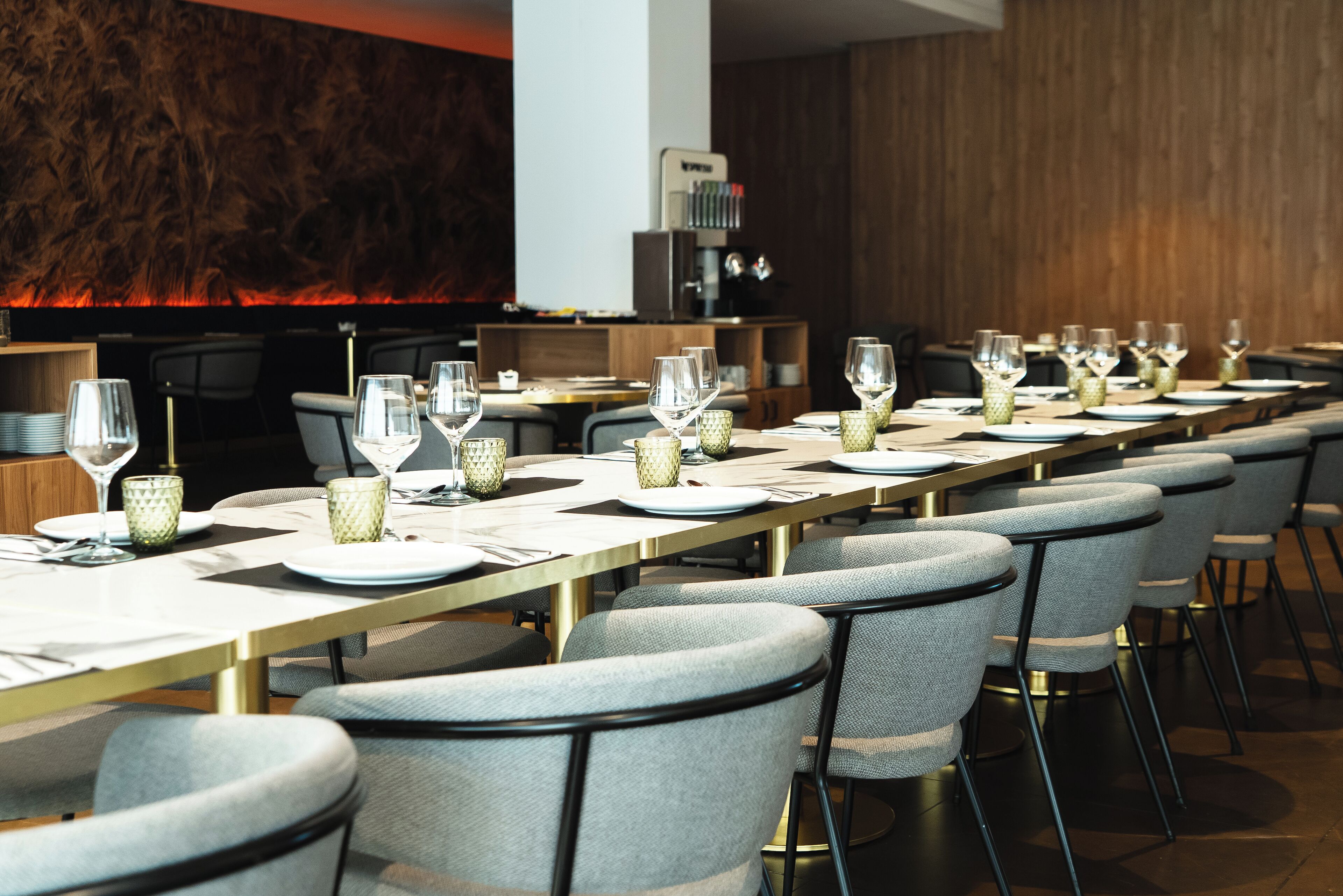 Una larga mesa de comedor dispuesta con sillas, copas y platos, en un interior moderno con paneles de madera y una chimenea.