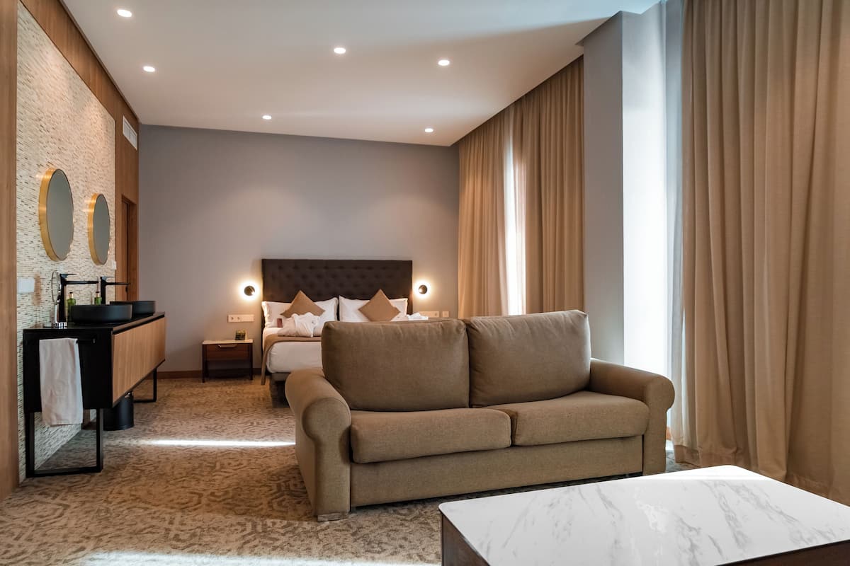 Una habitación de hotel moderna con una cama grande, un sofá, una mesita y un baño con espejo y lavabo.