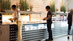 A buffet area with a patterned wall, potted plants, and a counter with stacked plates. - Hotel AJ Gran Alacant (Santa Pola)