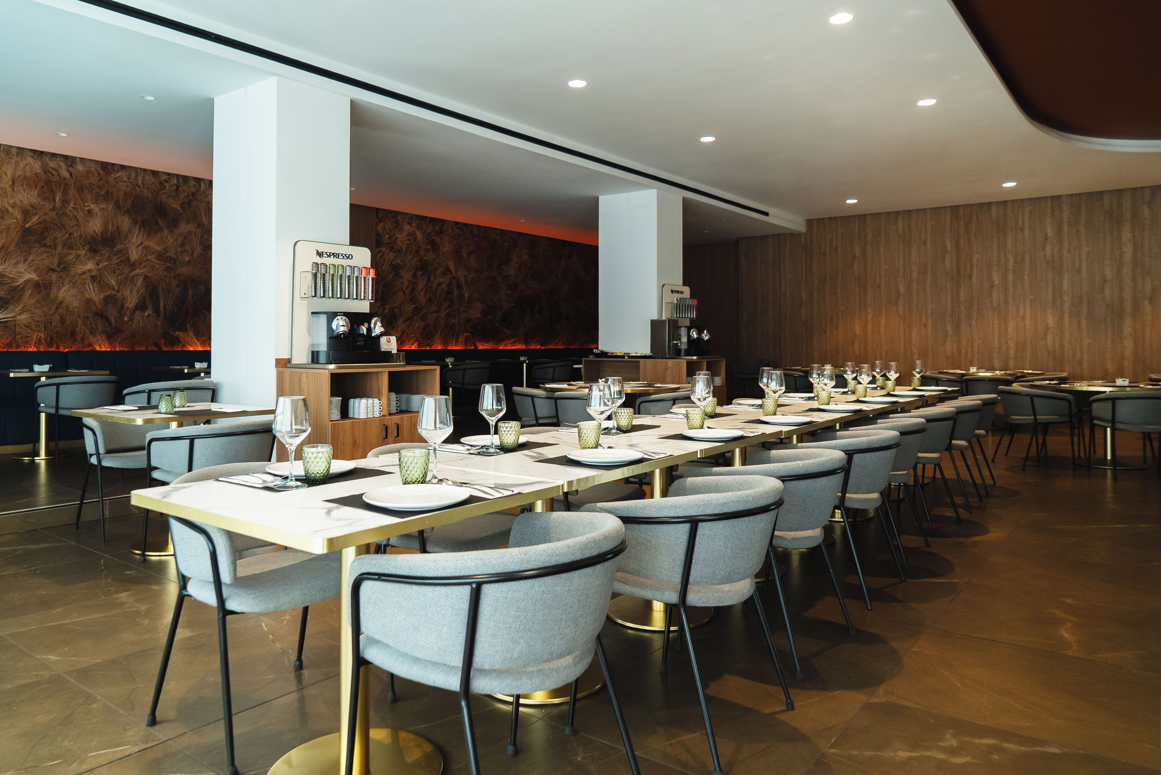A modern dining area with long tables, chairs, and a coffee machine.