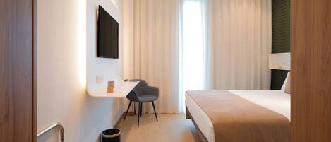 A hotel room with a bed, a desk, a chair, and a TV mounted on the wall.