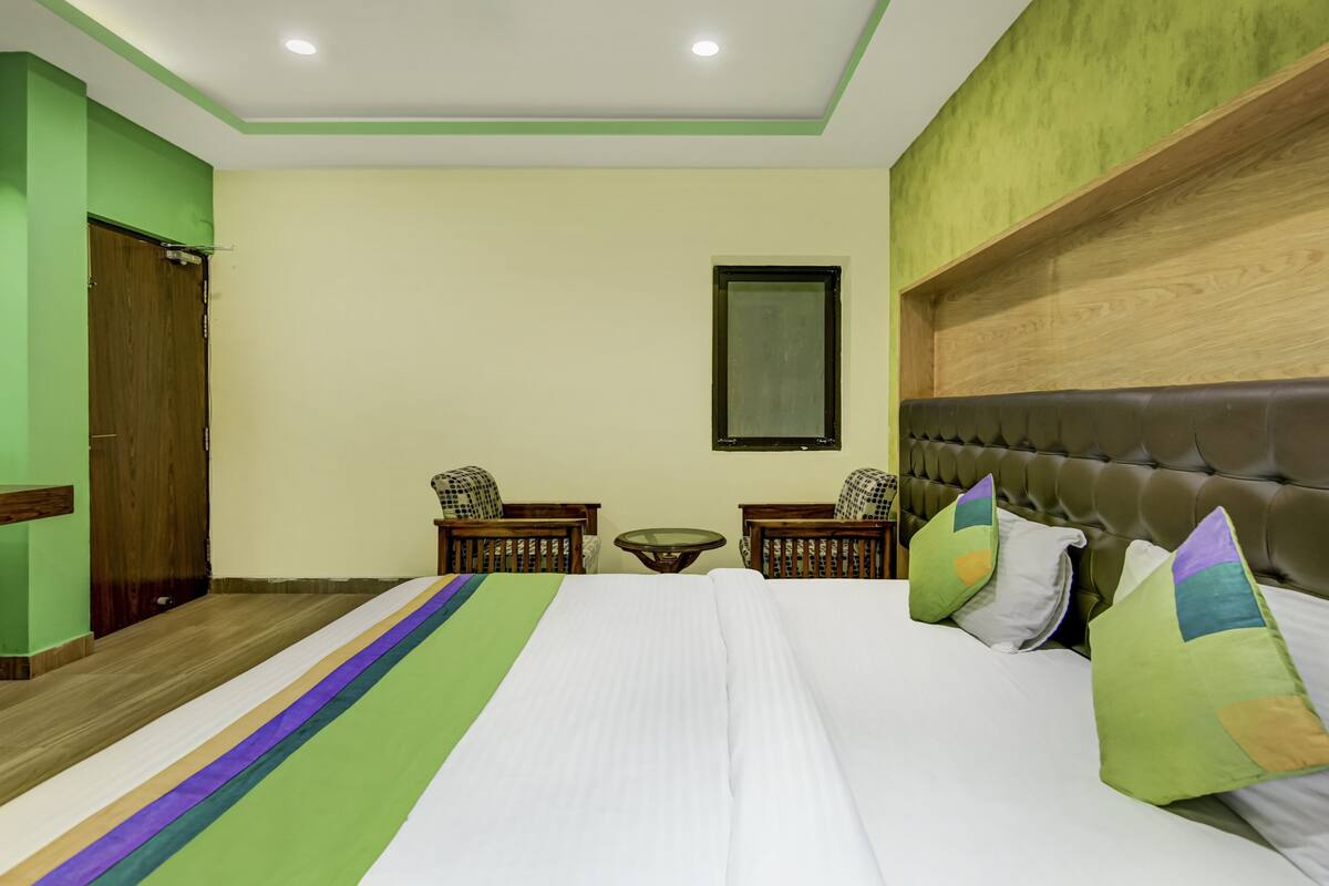 A hotel room with a large bed, two wooden chairs, a small table, and a mirror on the wall.