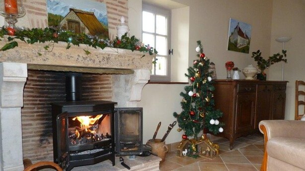 A cozy living room with a fireplace, a Christmas tree, and a stone fireplace surround. - Charming house in Lamonzie-Saint-Martin (Lamonzie-Saint-Martin)