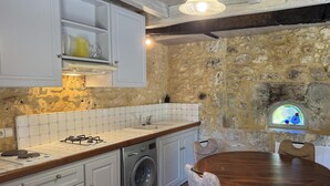 A kitchen with a stone wall, a washing machine, a dining table with chairs, and a hanging light fixture. - Authentic Stay in 17th Century Dovecote with Internet and Pets Allowed (Monsac)