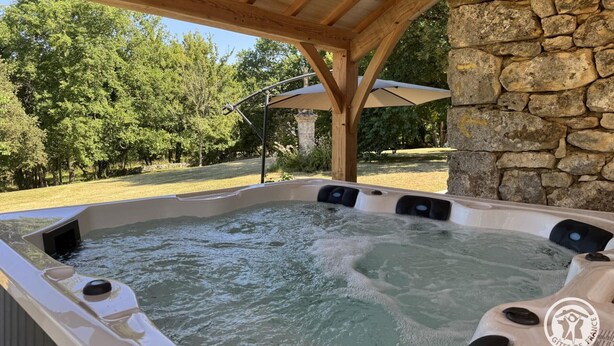 A hot tub under a wooden pergola with stone walls, surrounded by trees. - Authentic Stay in 17th Century Dovecote with Internet and Pets Allowed (Monsac)