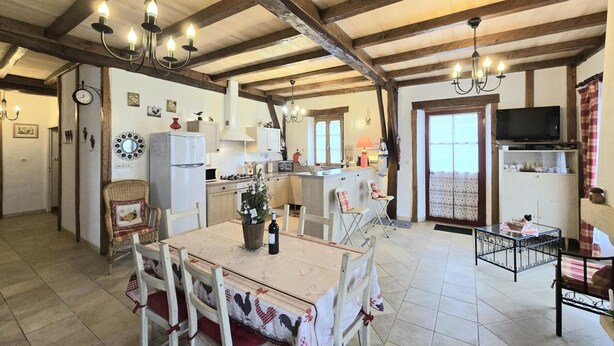 A rustic kitchen with wooden beams, a dining table with chairs, a TV, and a Christmas tree. - Périgord house with fireplace near Monpazier (Mazeyrolles)