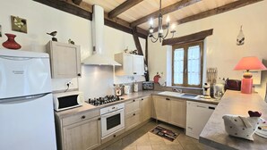 A kitchen with wooden beams, a gas stove, a refrigerator, a sink, and a window with curtains. - Périgord house with fireplace near Monpazier (Mazeyrolles)